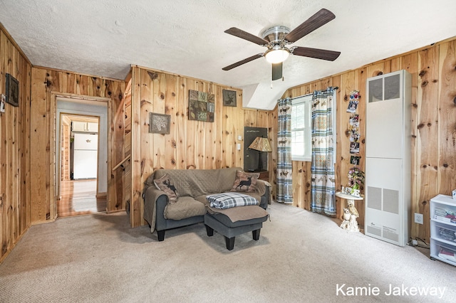 living area featuring ceiling fan, light carpet, a textured ceiling, and wooden walls