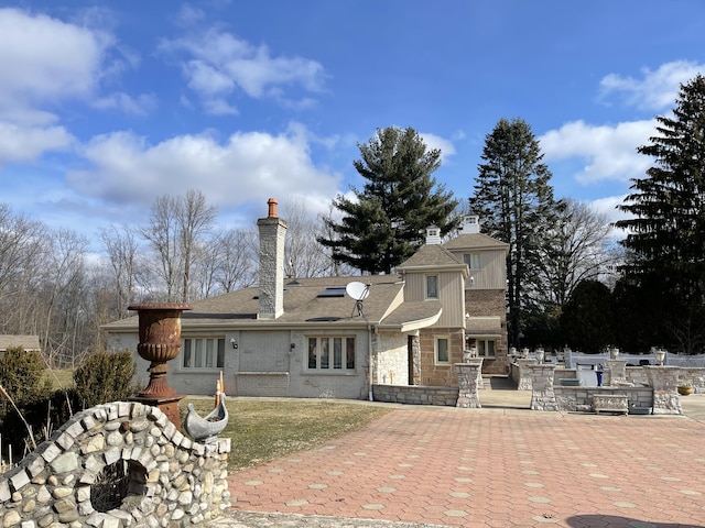 rear view of property featuring stone siding, a chimney, and a patio area