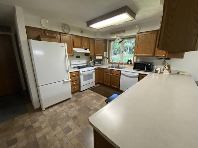 kitchen with white appliances, brown cabinetry, light countertops, under cabinet range hood, and a sink