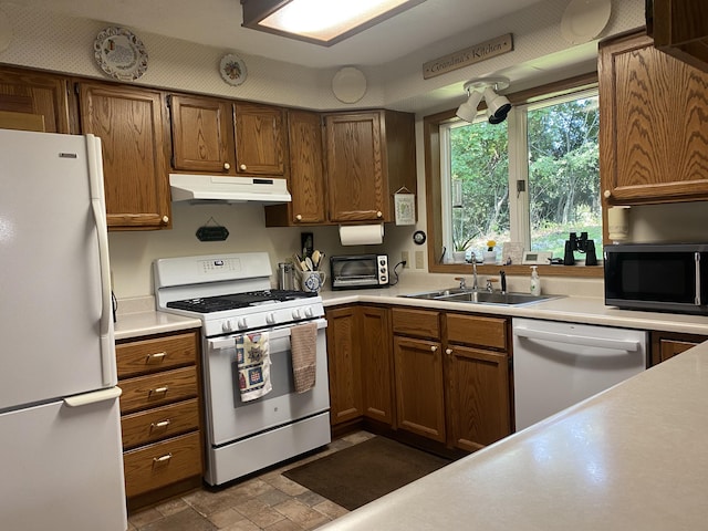 kitchen featuring brown cabinets, light countertops, a sink, white appliances, and under cabinet range hood