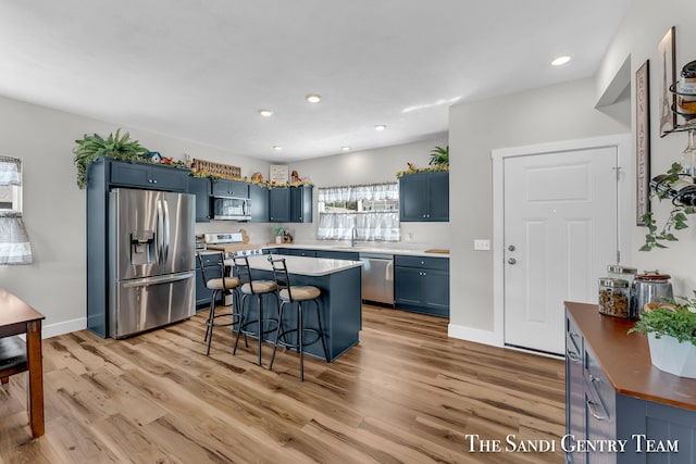 kitchen featuring blue cabinetry, light hardwood / wood-style flooring, a kitchen breakfast bar, and stainless steel appliances