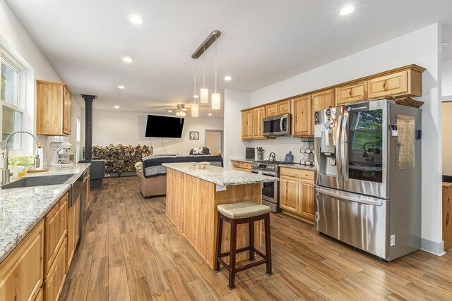 kitchen with appliances with stainless steel finishes, sink, light wood-type flooring, and light stone counters