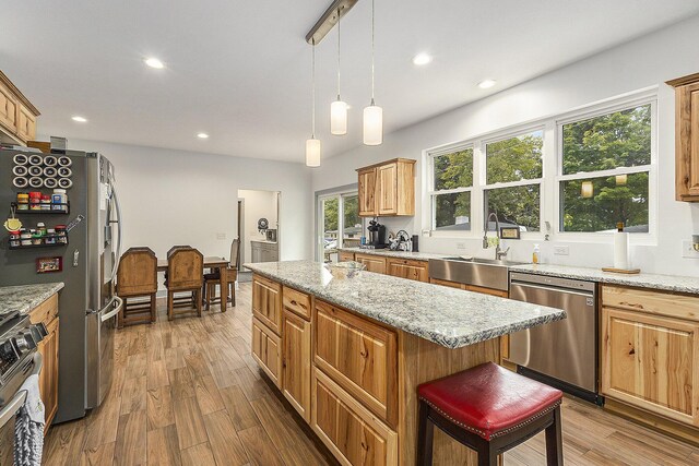 kitchen featuring stainless steel appliances, light hardwood / wood-style flooring, a kitchen bar, and light stone counters