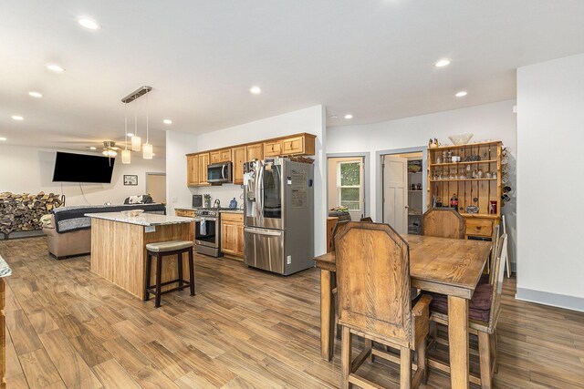 kitchen with a kitchen bar, appliances with stainless steel finishes, pendant lighting, light stone countertops, and light hardwood / wood-style floors