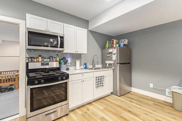 kitchen featuring appliances with stainless steel finishes, white cabinetry, sink, and light hardwood / wood-style floors