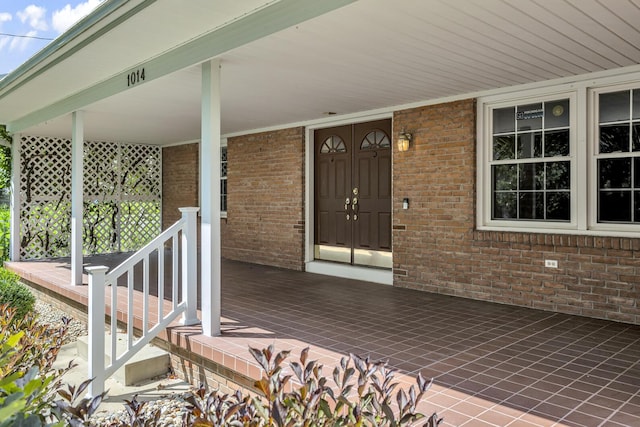 doorway to property featuring covered porch and brick siding