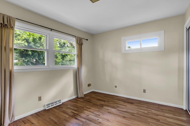 empty room with visible vents, plenty of natural light, baseboards, and wood finished floors