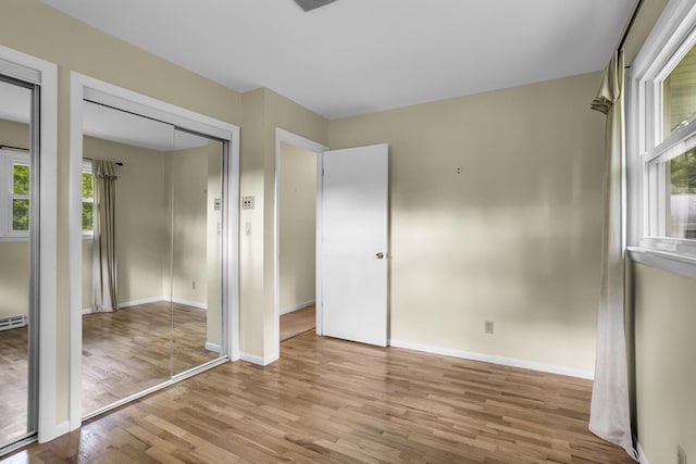 unfurnished bedroom with baseboards, baseboard heating, two closets, and light wood-style floors