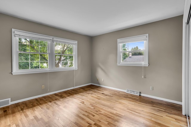 empty room with light wood-type flooring, visible vents, and baseboards