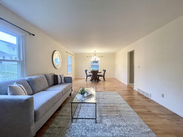 living area with a chandelier, visible vents, baseboards, and wood finished floors