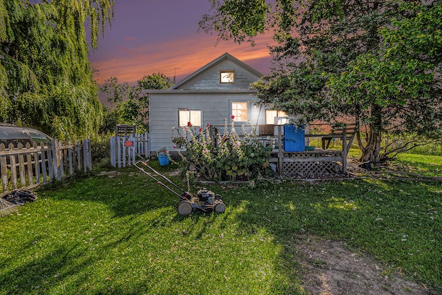 back house at dusk featuring a wooden deck and a yard