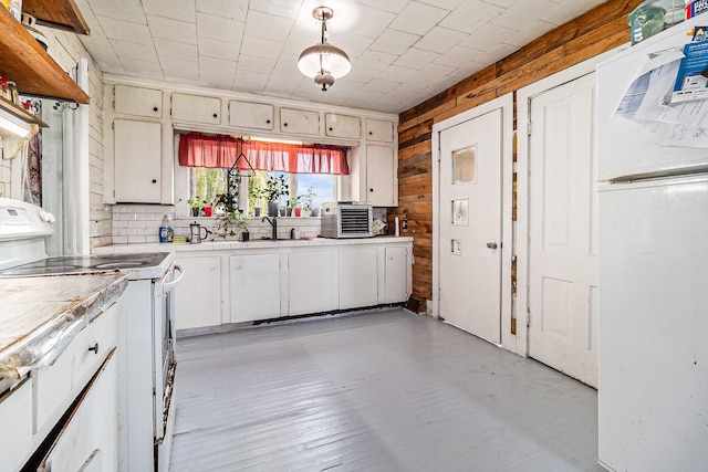 kitchen with wooden walls, decorative light fixtures, light wood-type flooring, white appliances, and sink