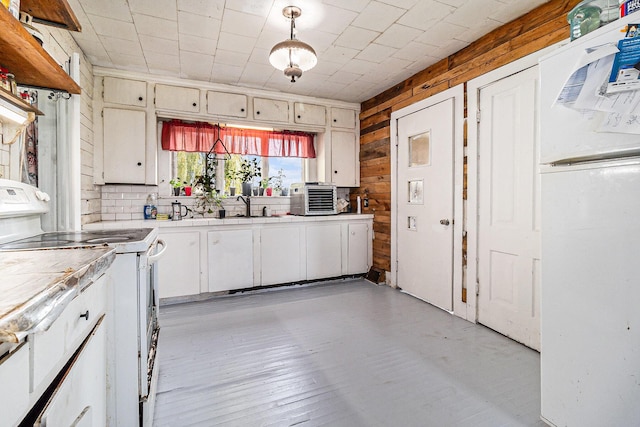 kitchen featuring light wood finished floors, decorative light fixtures, wood walls, white electric range, and a sink