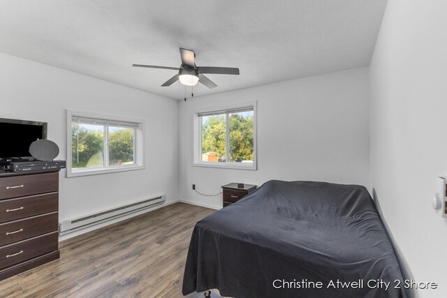 bedroom with baseboard heating, ceiling fan, hardwood / wood-style flooring, and multiple windows