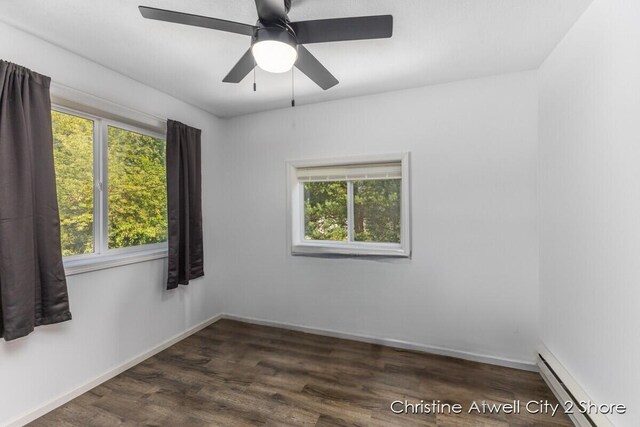 empty room with ceiling fan, dark wood-type flooring, a wealth of natural light, and a baseboard heating unit