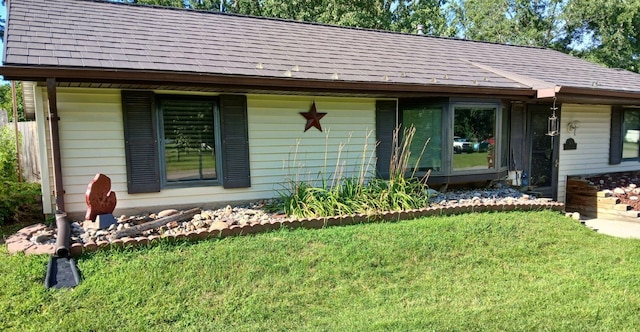 view of exterior entry with a lawn and roof with shingles