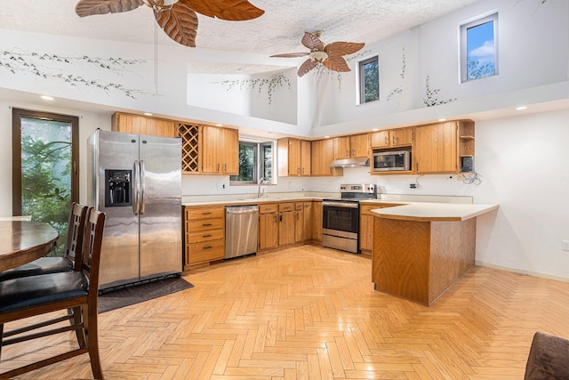 kitchen featuring appliances with stainless steel finishes, ceiling fan, a high ceiling, light parquet flooring, and kitchen peninsula