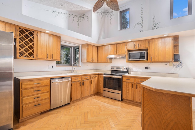 kitchen with light parquet floors, a towering ceiling, kitchen peninsula, stainless steel appliances, and sink