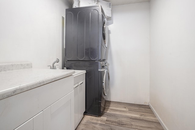 washroom with light hardwood / wood-style flooring, cabinets, and stacked washer / dryer