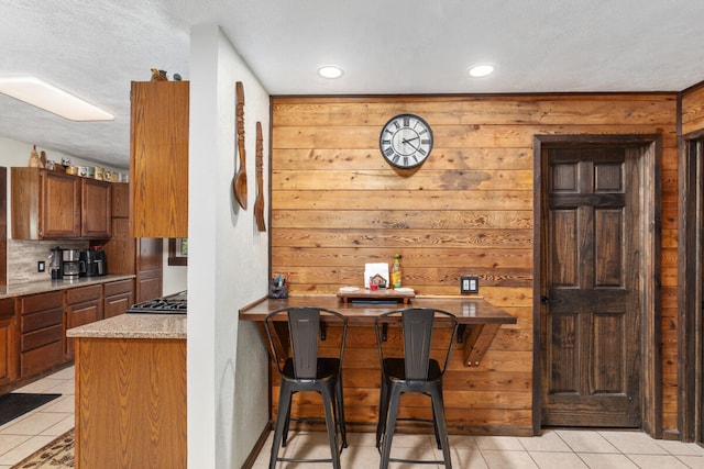 kitchen with light tile patterned flooring, a textured ceiling, gas cooktop, and a breakfast bar area