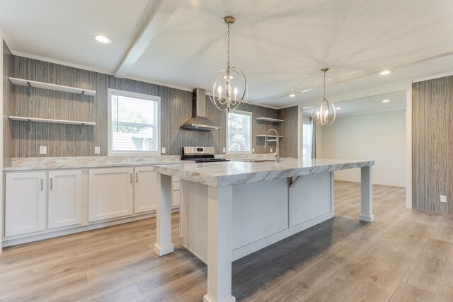 kitchen featuring white cabinets, wall chimney range hood, stove, a center island with sink, and light hardwood / wood-style floors