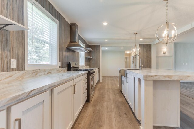 kitchen featuring stainless steel range with gas stovetop, wall chimney range hood, white cabinetry, and light hardwood / wood-style floors