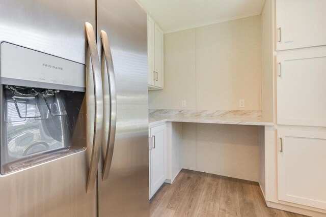 kitchen with stainless steel fridge, white cabinetry, light stone counters, and light hardwood / wood-style floors