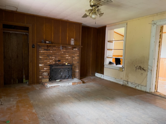 unfurnished living room featuring wood walls, a brick fireplace, and ceiling fan