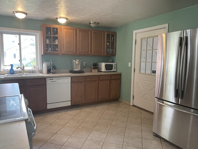 kitchen featuring white appliances, glass insert cabinets, brown cabinetry, and a sink