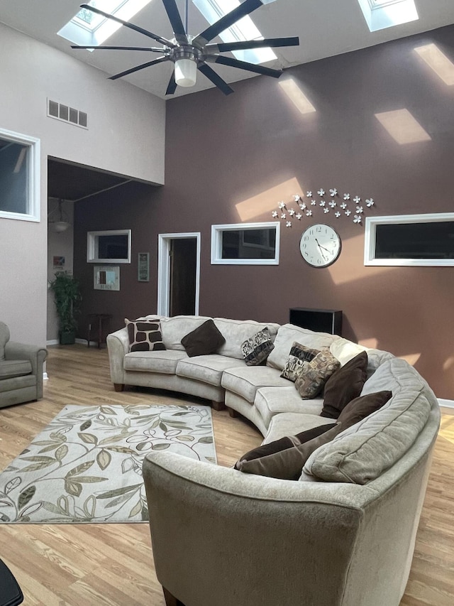 living room featuring ceiling fan, visible vents, wood finished floors, and a skylight