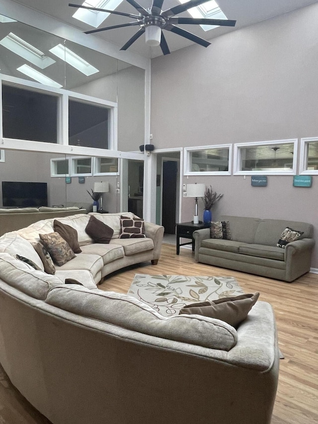 living room with ceiling fan, wood finished floors, high vaulted ceiling, and a skylight