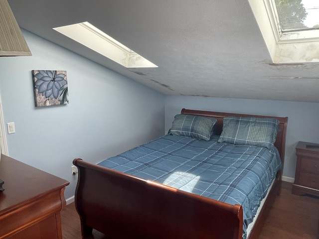 bedroom featuring baseboards, vaulted ceiling with skylight, and wood finished floors