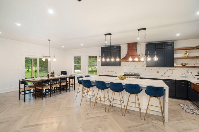 kitchen with backsplash, pendant lighting, a spacious island, light parquet flooring, and wall chimney exhaust hood