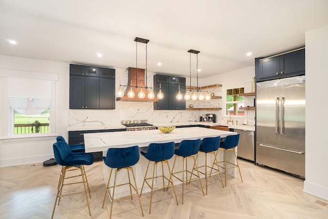 kitchen featuring wall chimney range hood, decorative backsplash, appliances with stainless steel finishes, light parquet floors, and a center island