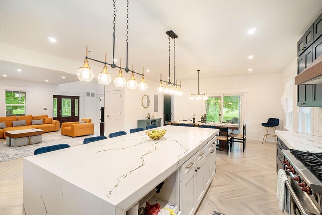 kitchen with stainless steel stove, light stone counters, light parquet flooring, a kitchen island, and hanging light fixtures