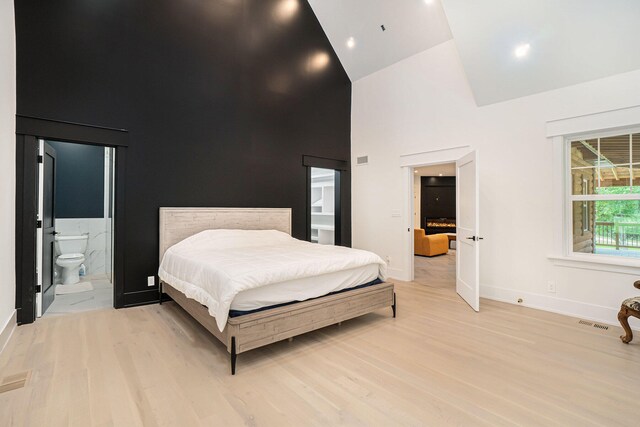 bedroom featuring ensuite bath, high vaulted ceiling, and light wood-type flooring