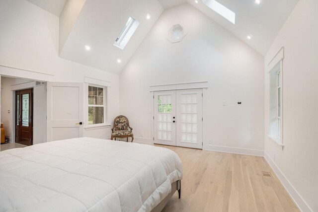 bedroom with high vaulted ceiling, light hardwood / wood-style floors, a skylight, and access to outside