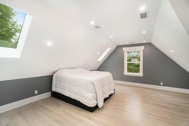 bedroom with vaulted ceiling with skylight and light hardwood / wood-style flooring