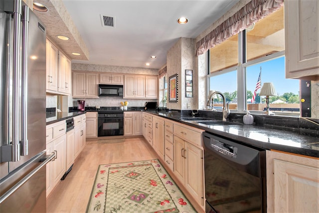 kitchen featuring dark stone counters, light brown cabinetry, light hardwood / wood-style floors, sink, and black appliances