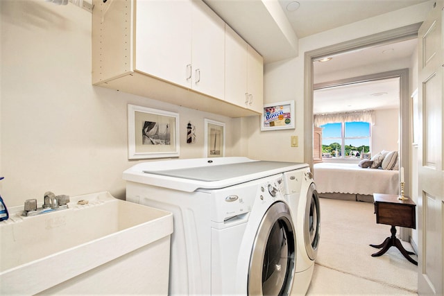 clothes washing area with sink, washing machine and dryer, light carpet, and cabinets