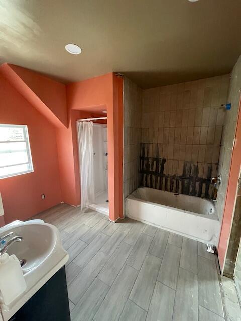 bathroom featuring wood finish floors, a stall shower, vanity, and a tub to relax in