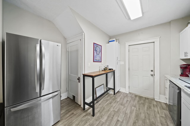 kitchen featuring white cabinets, appliances with stainless steel finishes, light stone countertops, vaulted ceiling, and light hardwood / wood-style floors