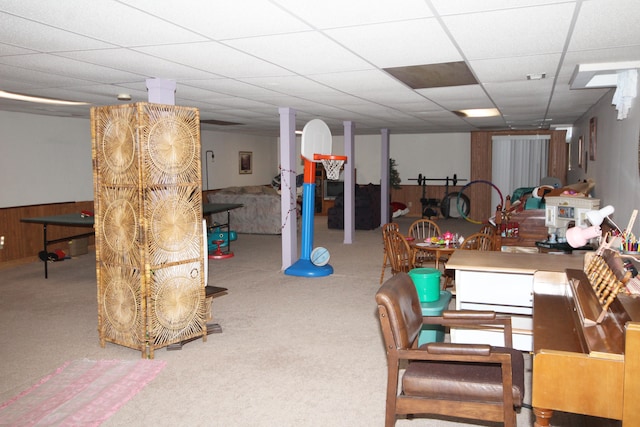 basement with a drop ceiling, wooden walls, and carpet flooring