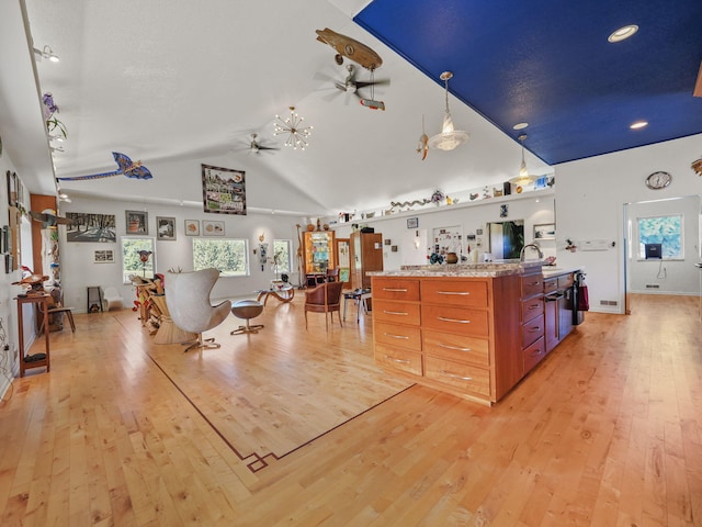 kitchen with decorative light fixtures, light stone counters, light hardwood / wood-style floors, vaulted ceiling, and ceiling fan