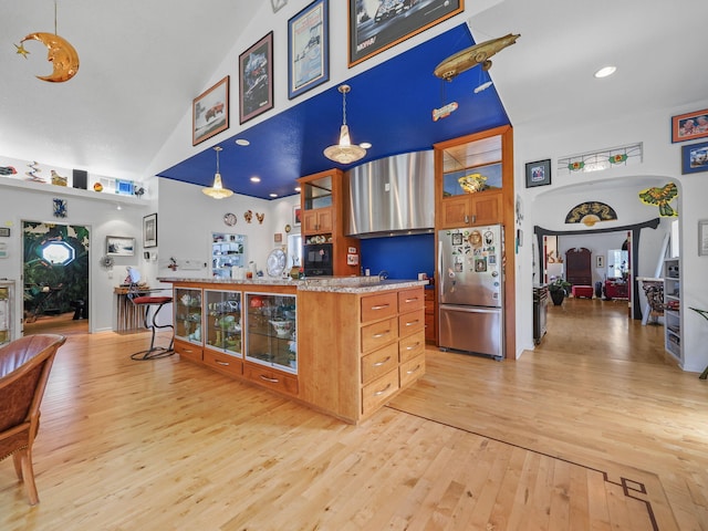 kitchen with high vaulted ceiling, light hardwood / wood-style floors, decorative light fixtures, a breakfast bar area, and stainless steel fridge