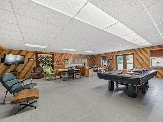 playroom with concrete floors, a drop ceiling, french doors, and wooden walls