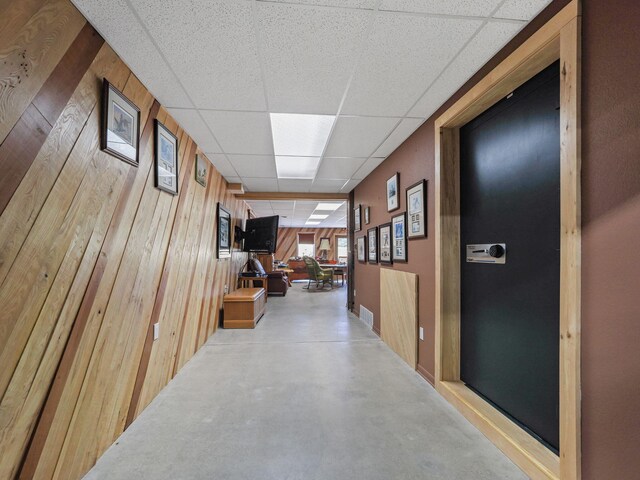 hallway with wood walls, concrete floors, and a drop ceiling