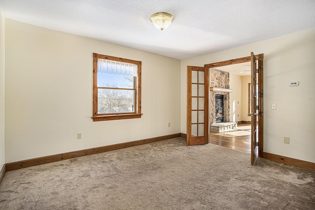 carpeted spare room featuring french doors, a fireplace, and a textured ceiling