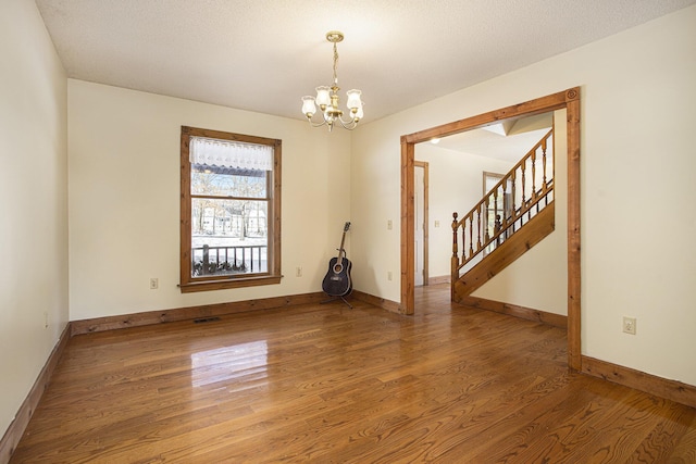 empty room with hardwood / wood-style floors, a textured ceiling, and a notable chandelier