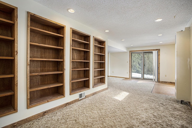 unfurnished living room featuring carpet, built in shelves, and a textured ceiling